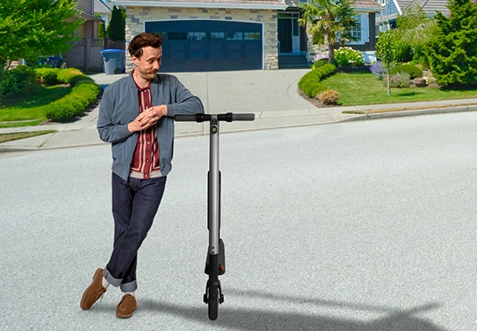 Ein lächelnder Mann mit einem E-Scooter auf der Straße.